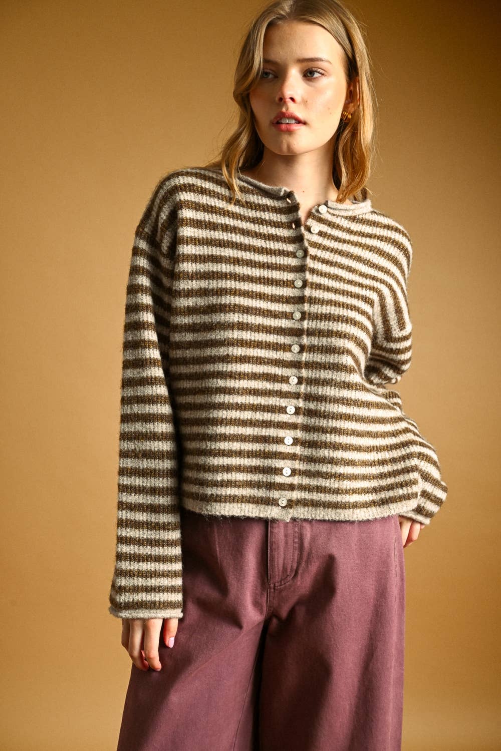 Woman wearing a striped sweater and purple pants against a beige background