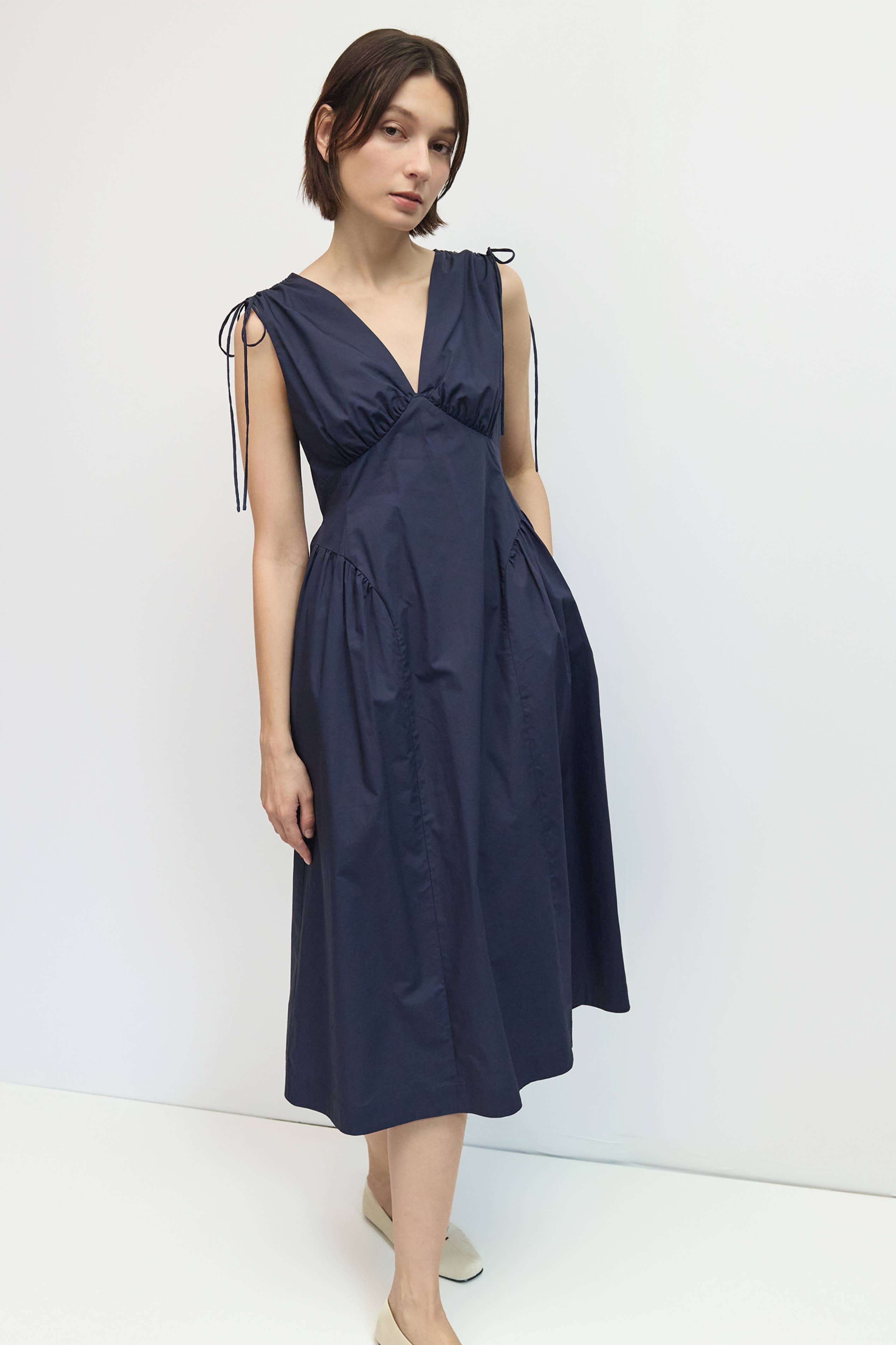Woman wearing a navy blue dress with ribbon straps against a white background