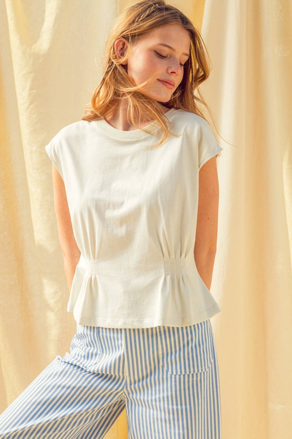 Woman wearing a white sleeveless top and striped pants against a beige curtain background