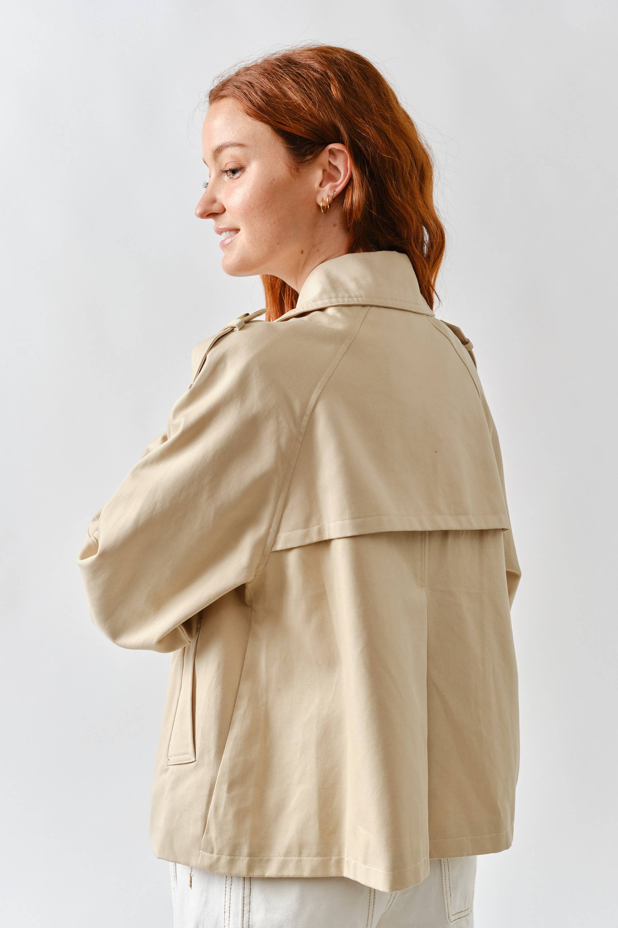 Woman wearing a beige trench coat against a white background
