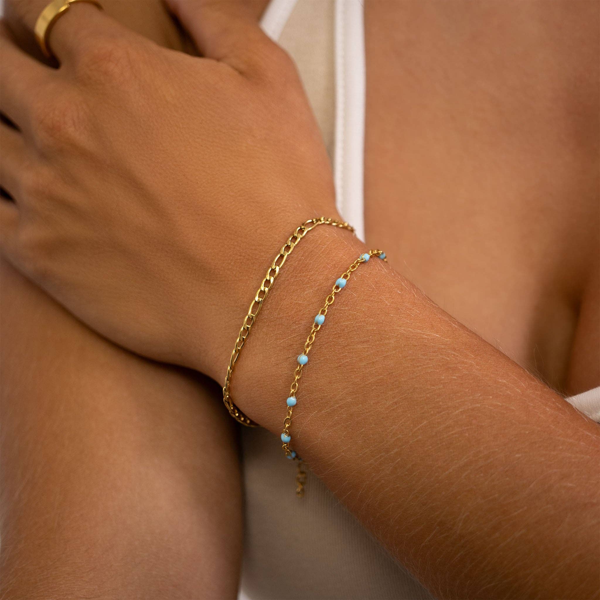 Close-up of a wrist wearing two gold bracelets with turquoise beads on a neutral background