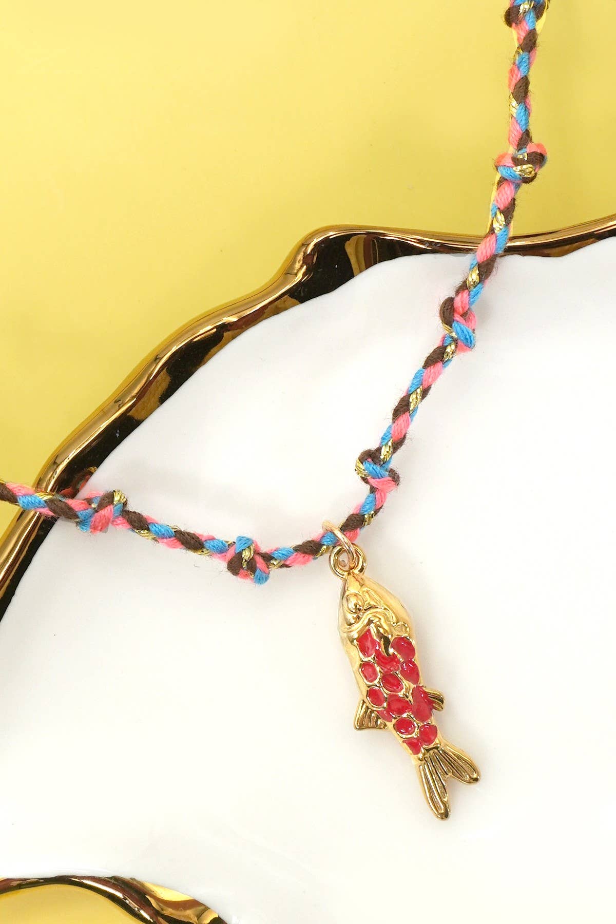 Necklace with a fish charm on a white surface with a gold leaf background
