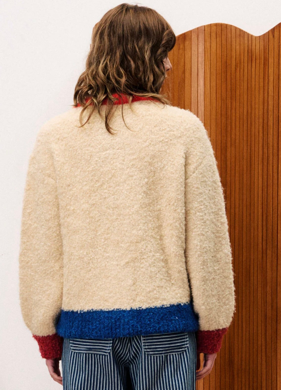 Person wearing a cream sweater with red cuffs and blue hem