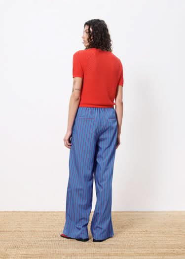 Woman facing away wearing red top and blue pants with red vertical stripes all over 