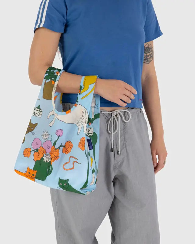 Model in white background holding BAGGU reuse-able light blue bag design with big colorful and nature flowers