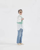 Model wearing white top and jeans holding BAGGU Green gingham nylon shoulder bag sitting against white background 