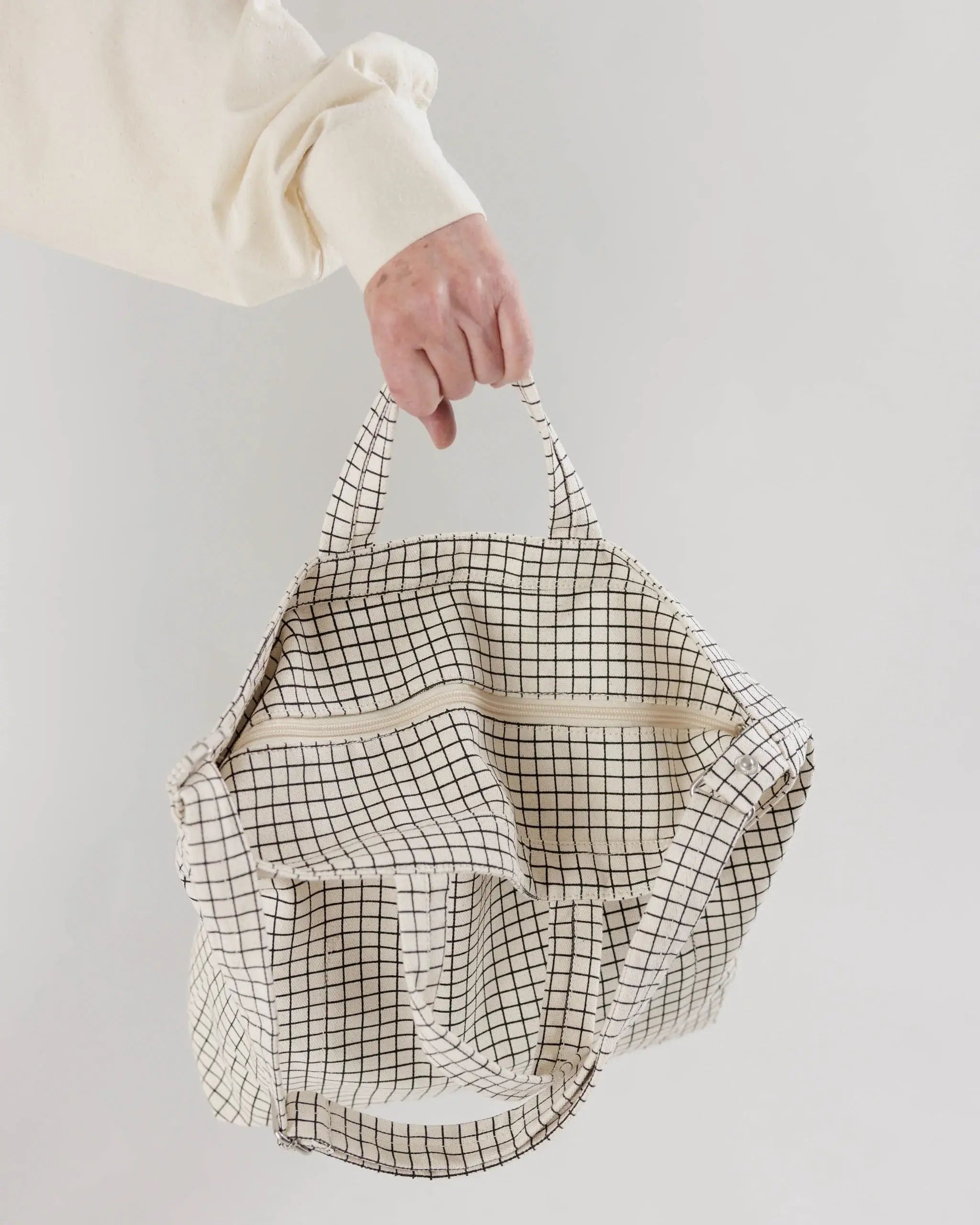 Shot of BAGGU zipper details on white background. BAGGU bag is a square tote bag with adjustable strap with white with black grid line design 