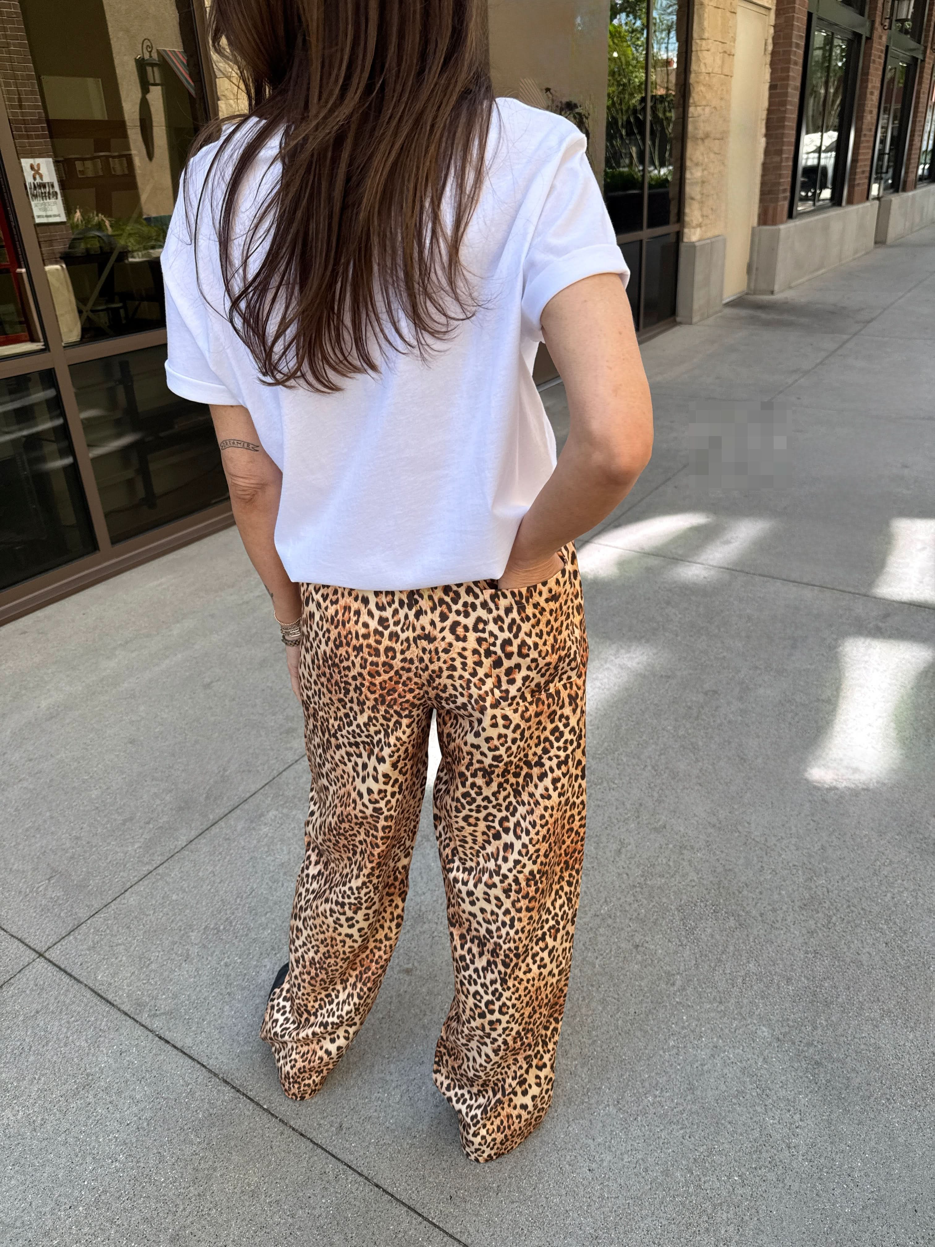 Person wearing a white t-shirt and leopard print pants standing on a sidewalk.