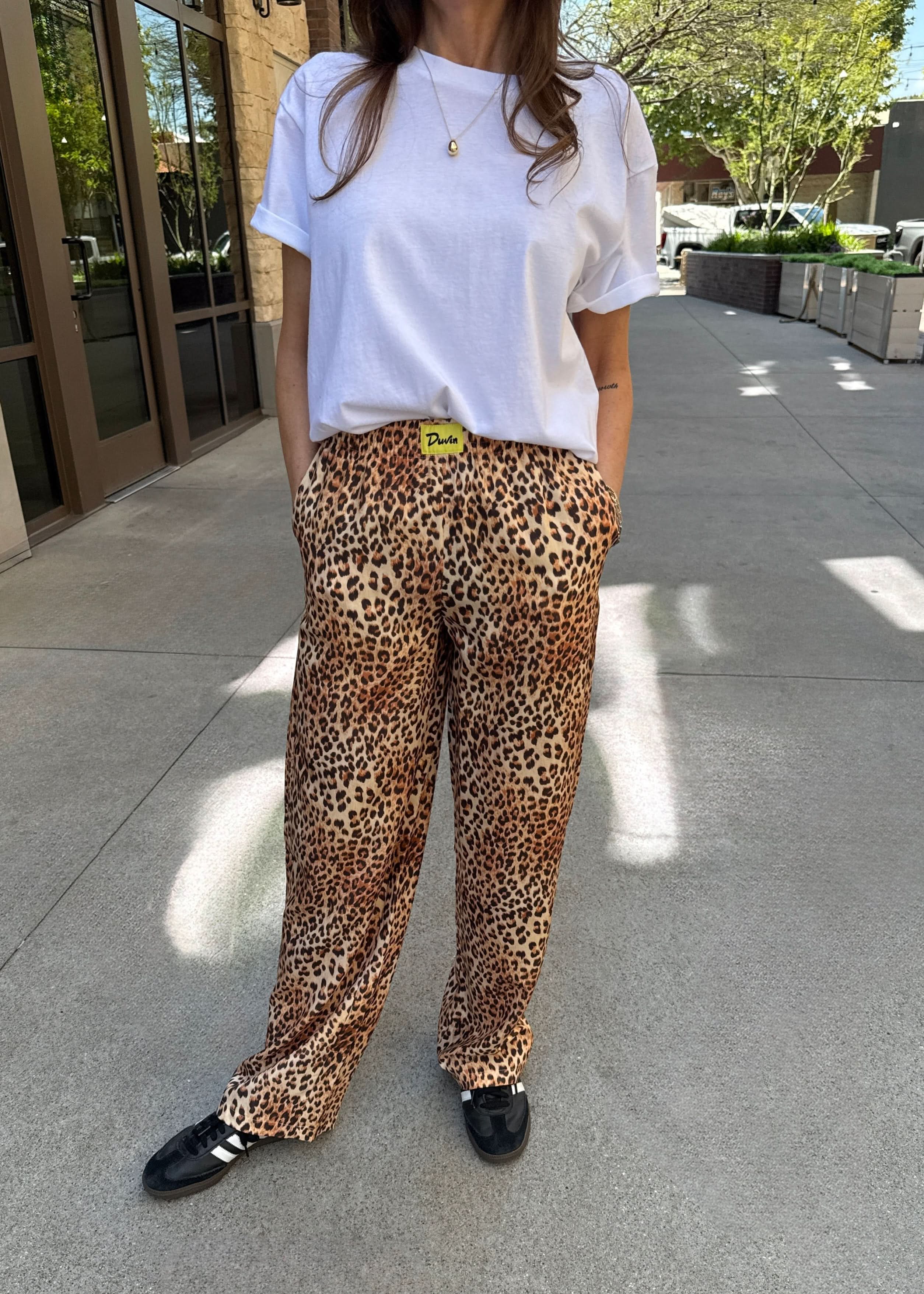 Person wearing a white t-shirt and leopard print pants on a sidewalk.