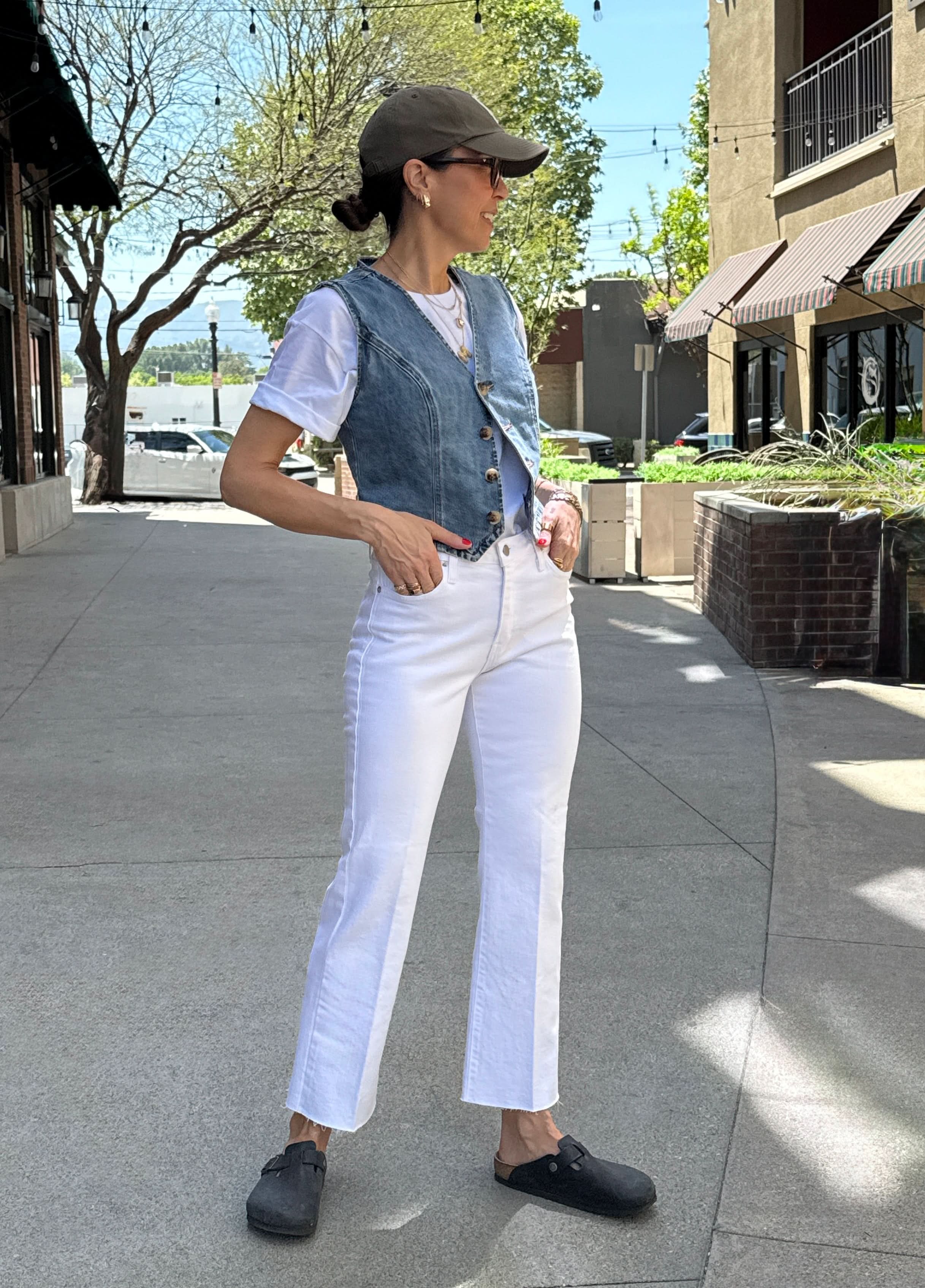 Person wearing a denim vest, white shirt, and white pants on a sidewalk.