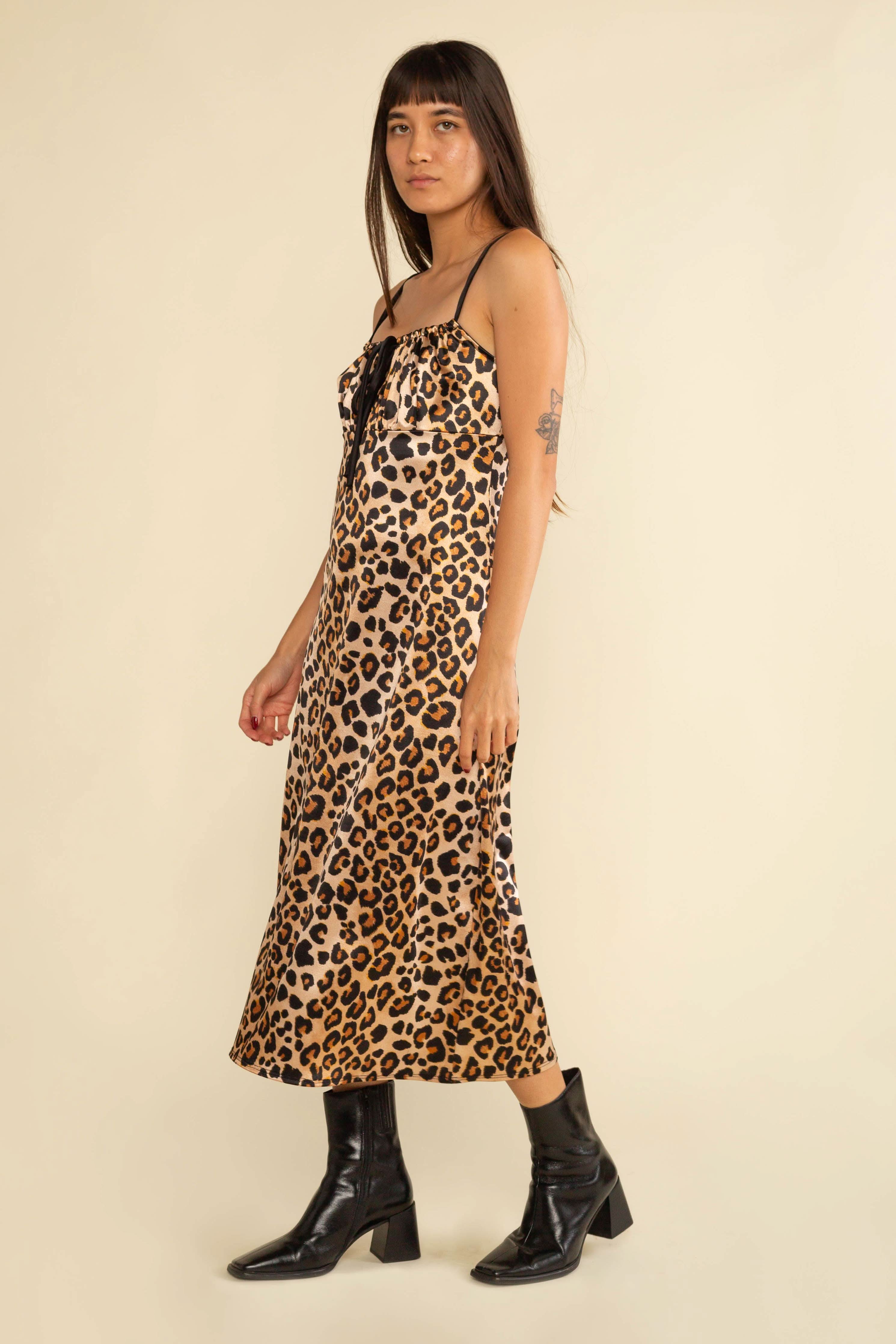Woman wearing a leopard print dress with black boots on a beige background