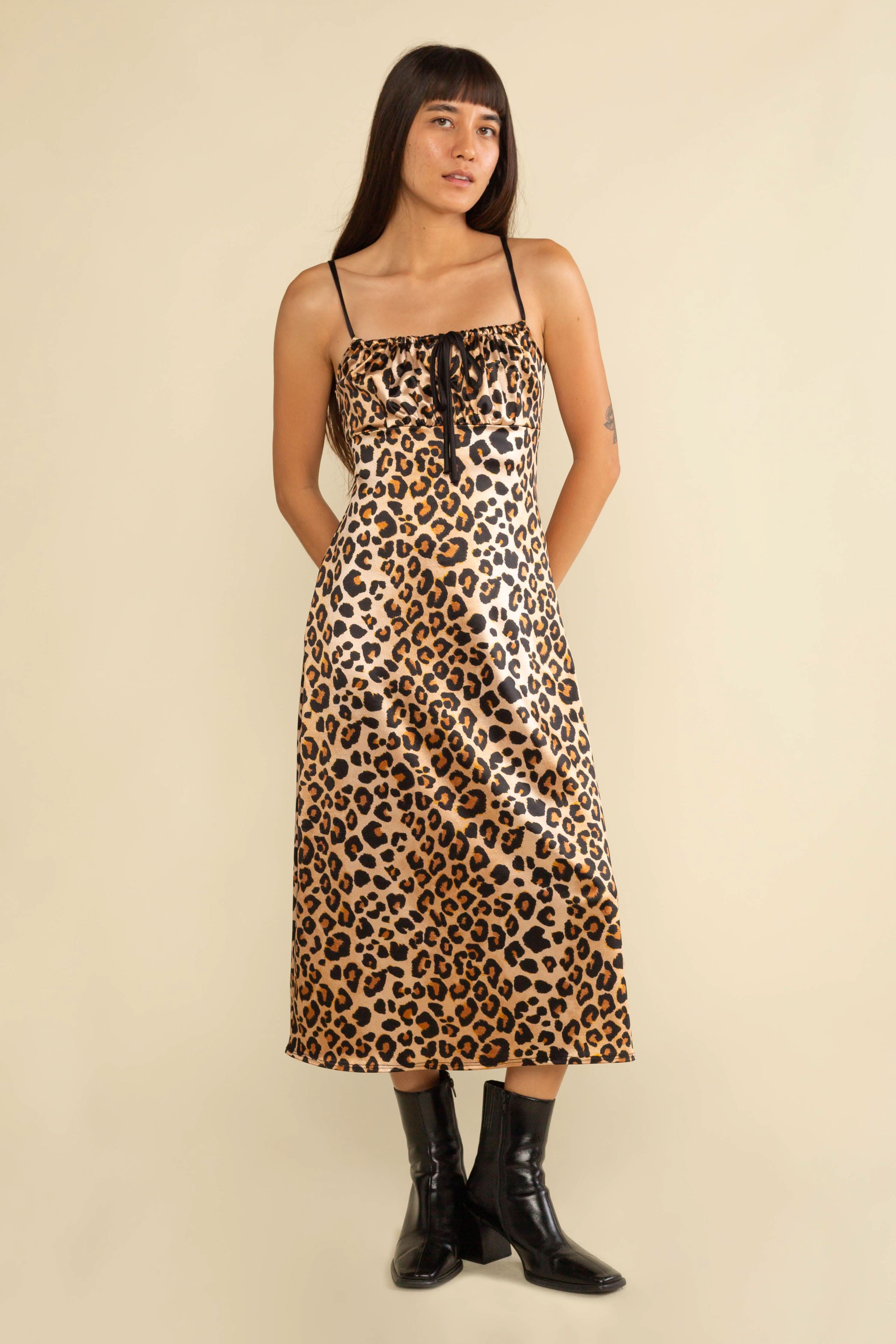 Woman wearing a leopard print dress with black boots on a beige background