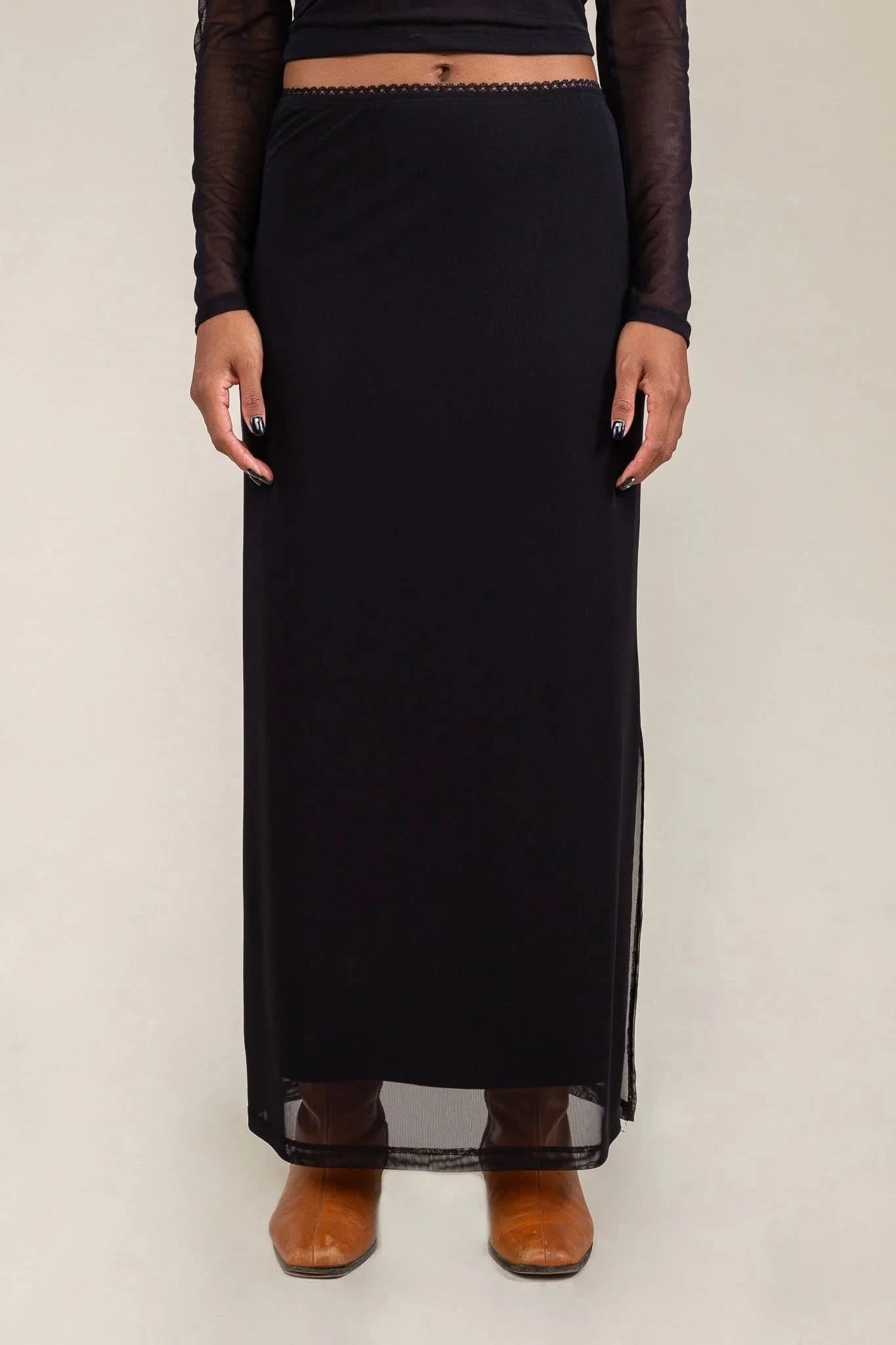 Person wearing a long black skirt with sheer panels on a plain background