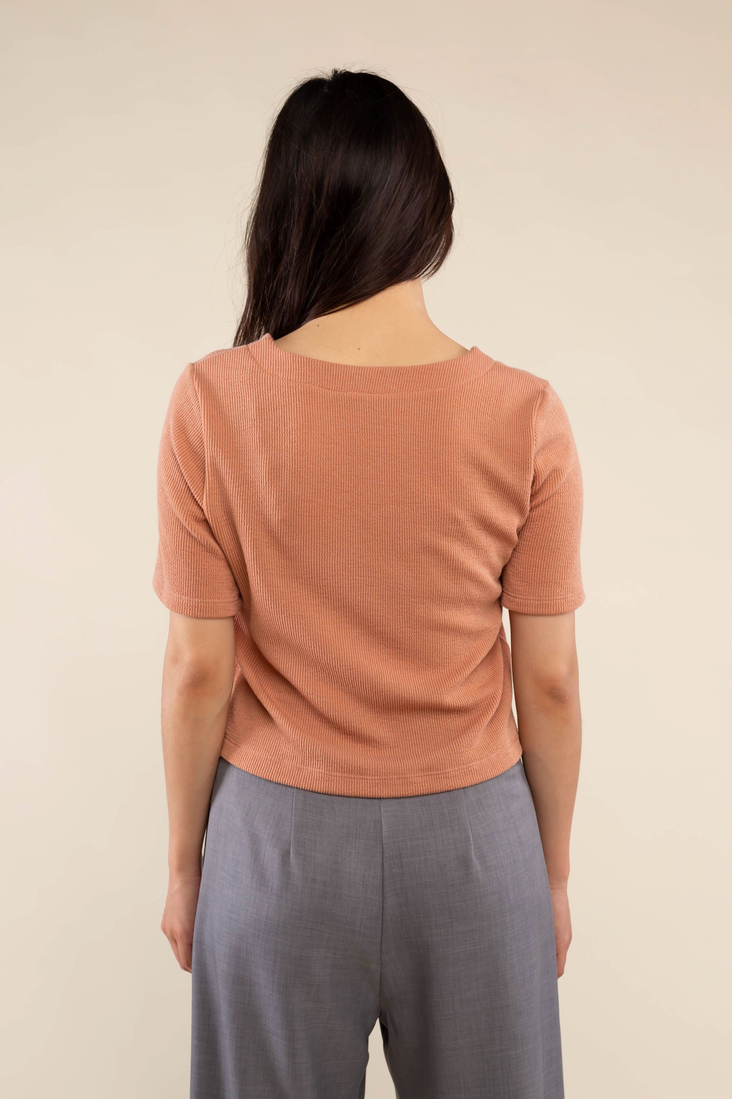 Woman wearing brick colored, ribbed, button down, short sleeve blouse top and grey pants 