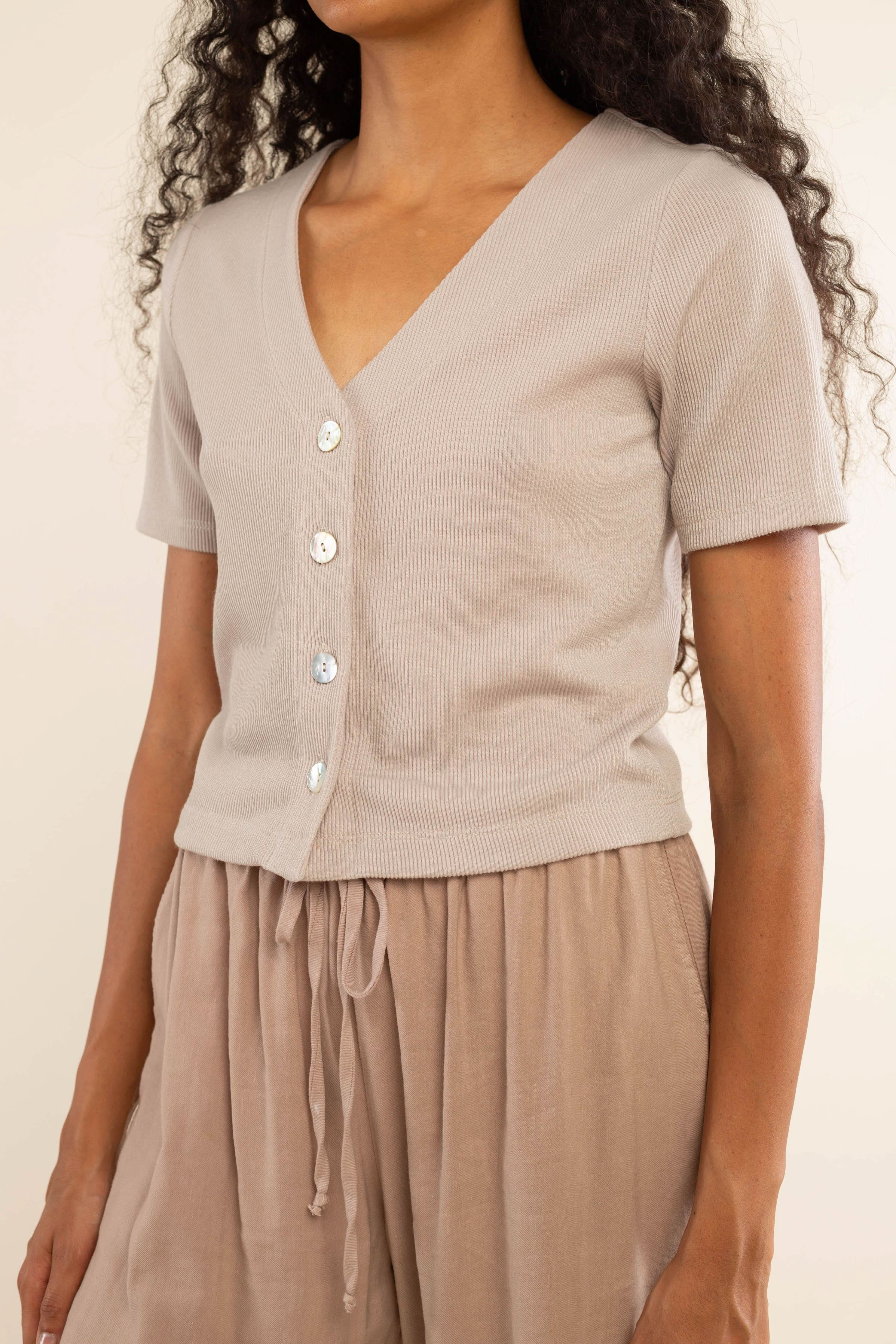 Woman wearing oat colored, ribbed, button down, short sleeve blouse top and beige pants 