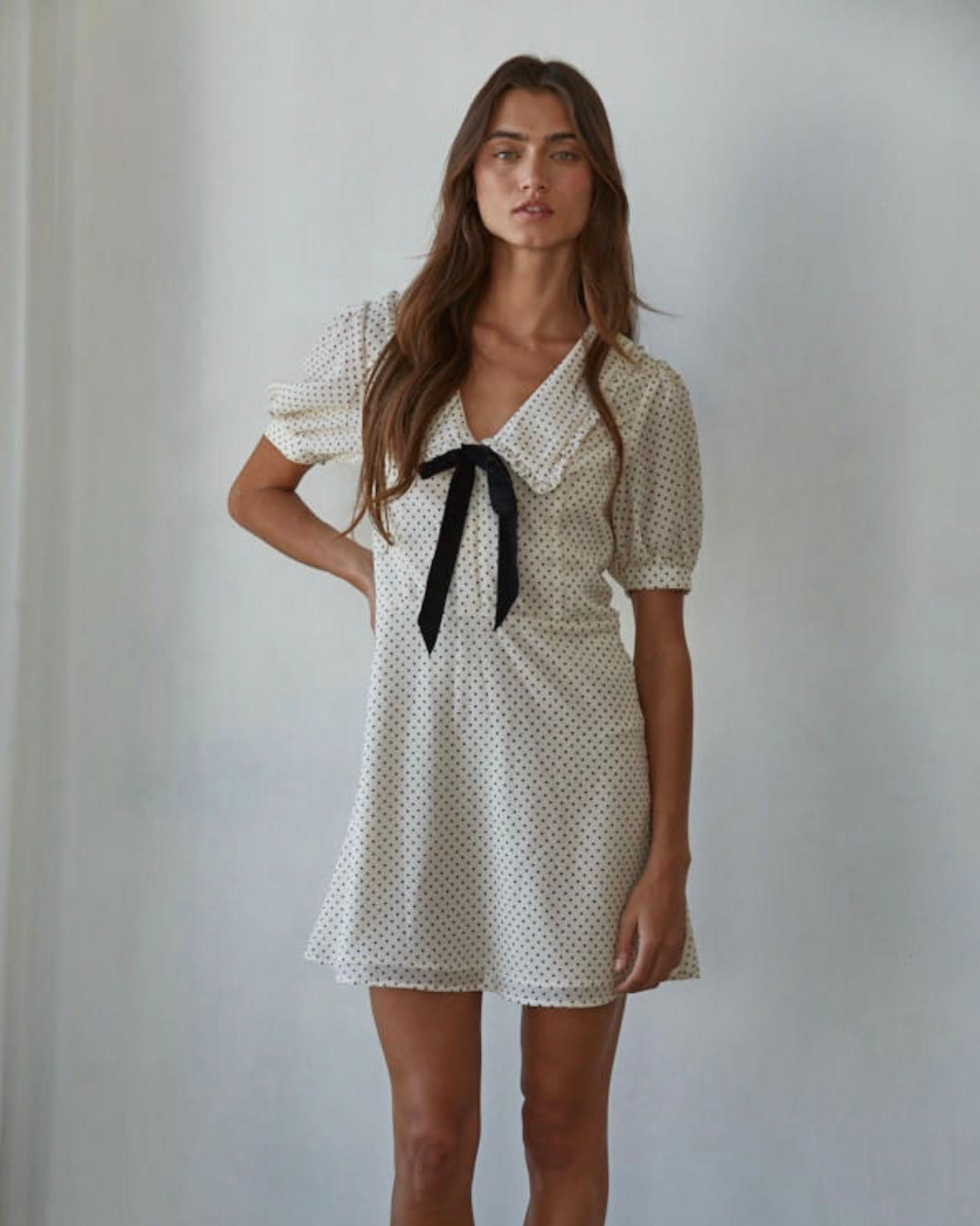 Woman wearing a white polka dot dress with a black ribbon against